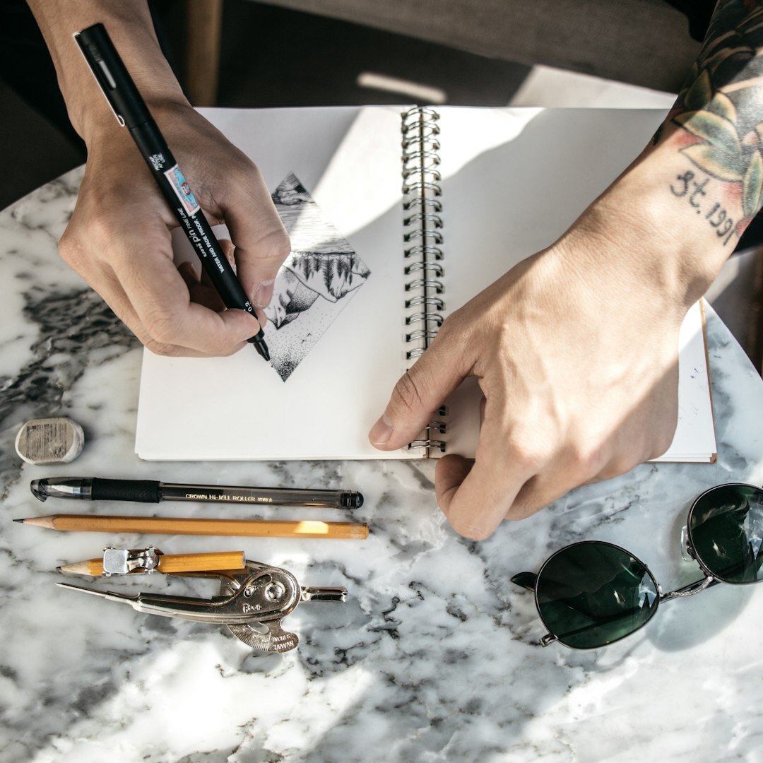 Close-up of hands writing in a notebook with a cup of coffee nearby